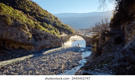 People crossing the Kadiut Bridge in Benje, Permet, Albania. Ancient stone bridge. Beautiful natural wonders. Holidays and leisure time. Fisherman fishing in the river. Natural thermal baths. - Powered by Shutterstock