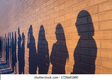 People crowd shadows lined up against a red brick wall. They are in a queue for changes in life. Social distance, covid and immigration issue concept - Shutterstock ID 1728681880