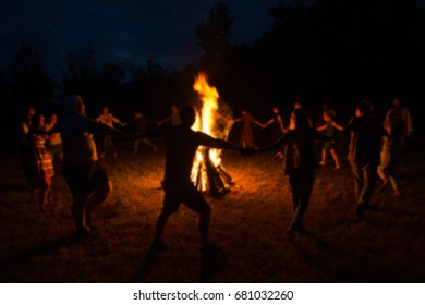 People dance around the campfire. Blurred silhouettes of people dance around the fire.
