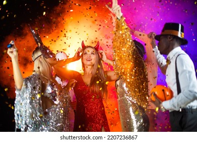 People Dance At Halloween Party With Champagne Glasses. Friends In The Costumes In Nightclub