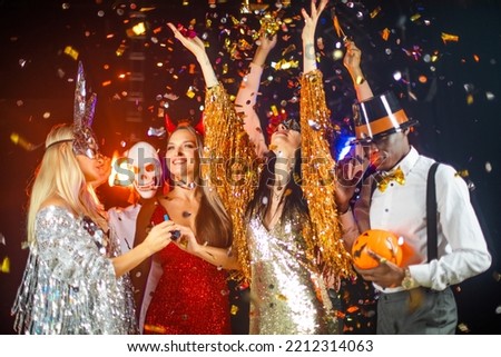 People dance at Halloween party with champagne glasses. Friends in the costumes in nightclub