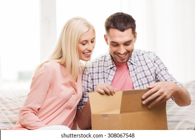 People, Delivery, Shipping And Postal Service Concept - Happy Couple Opening Cardboard Box Or Parcel At Home