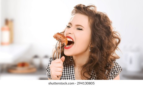 people, diet, culinary and food concept - hungry young woman eating meat on fork over kitchen background