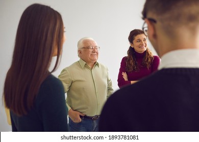 People Of Different Ages Gathering Together And Talking. Happy Senior Man Smiling And Laughing Having Conversation With Young Men And Women In Group Therapy Session Or Community Club Meeting