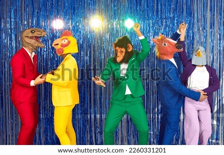 People in different animal disguises having fun at costume party. Group of happy people in bright suits and funny silly dinosaur, bird, ape, horse and dove masks dancing on blue foil fringe background