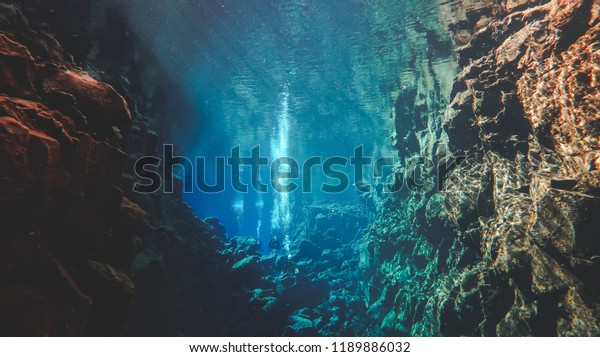 People divers diving in a famous crack between\
two tectonic plates in Iceland Silfra hall blue deep underwater\
water colors colorful lava rock formations, crystal clear sky\
diving floating air\
bubbles