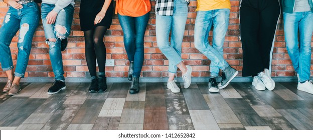 People Diversity. Cropped Shot Of Men Women Legs In Jeans. Group Standing Leaning Against Brick Wall. Relaxed Millennials