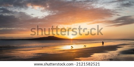 People and dog playing at Milford beach at sunrise, Rangitoto Island in the distance, Auckland.