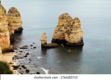 People Doing Kayak Sport Around Algarve Water Cliffs In Portugal, With Beautiful Sea, And Beach