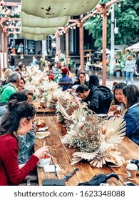 People Eating Along The Long Table. Street Food Market Festival Outdoors. Beautiful Trendy Decorated Wooden Table At City Food Court. Mobile Photography. Moscow, Russia - August 17, 2019