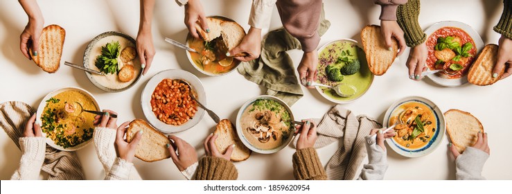 People Eating Autumn And Winter Creamy Vegan Soups. Flat-lay Of Peoples Hands, Soup Plates And Bread Slices Over Plain White Table Background, Top View. Fall And Winter Food Menu, Vegetarian Food