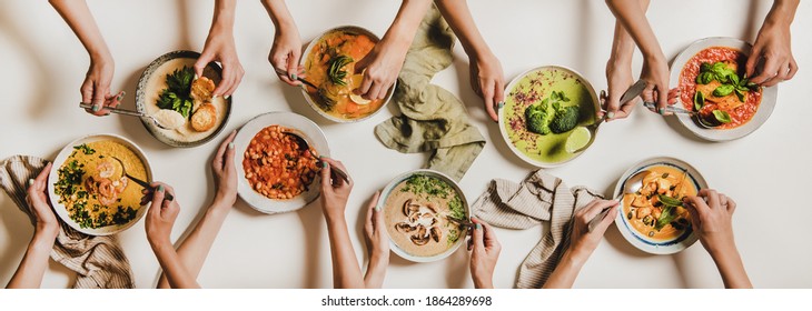 People Eating Autumn And Winter Creamy Vegan Soups. Flat-lay Of Peoples Hands With Soup Plates And Bread Slices Over Plain White Table Background, Top View. Fall And Winter Food Menu, Vegetarian Food