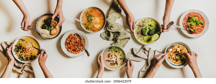 People Eating Autumn And Winter Creamy Vegan Soups. Flat-lay Of Peoples Hands With Homemade Soup And Bread Slices Over White Table Background, Top View. Fall And Winter Food Menu, Vegetarian Food