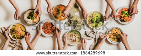 People eating Autumn and Winter creamy vegan soups. Flat-lay of peoples hands with soup plates and bread slices over plain white table background, top view. Fall and Winter food menu, vegetarian food