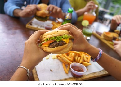 People Eating Burger In A Restaurant With Friends In Background