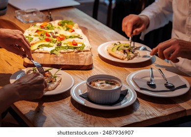 People eating flatbread pizza at a wooden table - Powered by Shutterstock