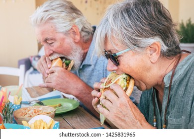 People Eating Hamburger Junk Food - Couple Of Senior Man And Woman With Fast Food Lunch Time - Close Up Of Elderly No Healthy Lifestyle - Tasty Sandwich Full Of Everything