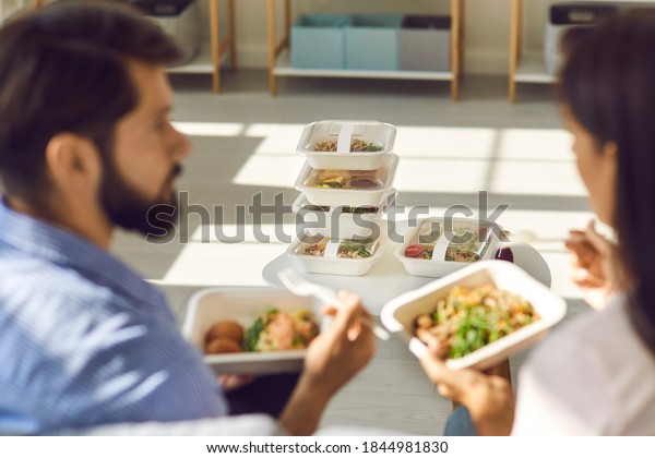 People eating healthy food at home or in office and\
discussing set of meals for the whole day. Stack of ordered and\
delivered takeaway containers with fresh breakfast, lunch and\
dinner in soft focus