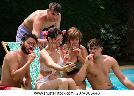People eating strawberry popsicles and taking a selfie near by a swimming pool.