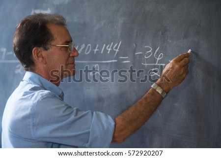 People and education. Teacher writing on math equation on blackboard during lesson.