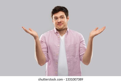 people, emotion and expression concept - young man shrugging over grey background