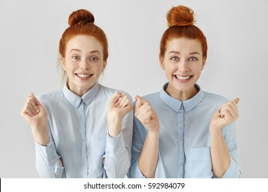 People, emotions and feelings. Two attractive happy young redhead women with hair knots wearing light-blue shirts having excited and winning looks, cheering, celebrating their success or victory