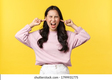 People Emotions, Lifestyle And Fashion Concept. Distressed And Mad Young Asian Woman Shouting With Closed Eyes And Outraged Face, Shut Ears, Unwilling To Listen, Yellow Background