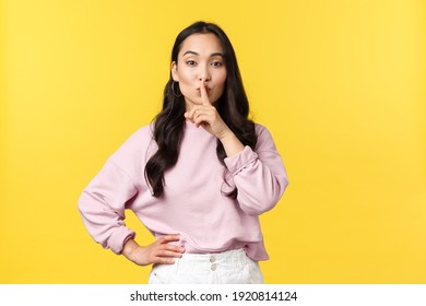 People emotions, lifestyle and fashion concept. Stylish attractive asian woman hush, say shhh as asking keep secret or be quiet, press finger to lips shushing, standing yellow background