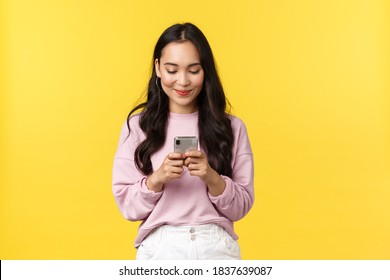 People emotions, lifestyle leisure and beauty concept. Smiling attractive asian woman using mobile phone, shopping online or messaging, texting friend, looking at smartphone screen pleased