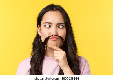 People emotions, lifestyle leisure and beauty concept. Close-up of playful funny asian girl fool around, make fake moustache out of hair and squinting, grimacing over yellow background - Shutterstock ID 1837639144