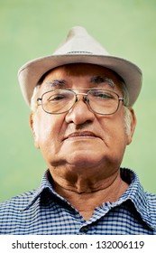 People And Emotions, Portrait Of Serious Senior Hispanic Man With Glasses And Hat Looking At Camera Against Green Background