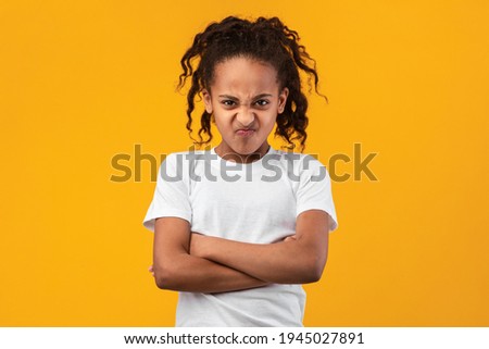 People Emotions, Teen Maximalism Concept. Portrait of offended young black girl posing with folded arms, standing isolated on yellow studio wall. Angry lady holding hands crossed, looking at camera