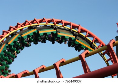 People Enjoying The Thrill Of A Roller Coaster Going Through A Loop At High Speed On A Clear Summer Day. 