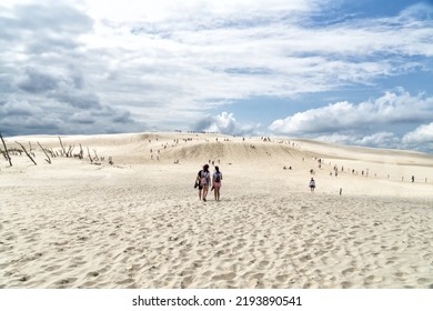People explore in Lacka dune in Slowinski National Park in Poland. Traveling dune in sunny summer day. Sandy beach and and blue sky with white clouds.