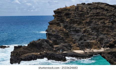 People exploring the rocky coastline and cliffs by the ocean on a sunny day, with clear blue water and sky. - Powered by Shutterstock