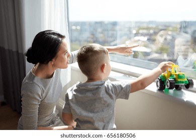 People And Family Concept - Happy Mother And Little Son With Toy Car Looking Through Window At Home