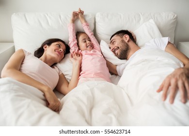 people, family and morning concept - happy child with parents waking up in bed at home