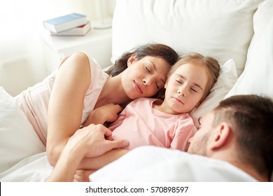 people, family and rest concept - happy child with parents sleeping in bed at home