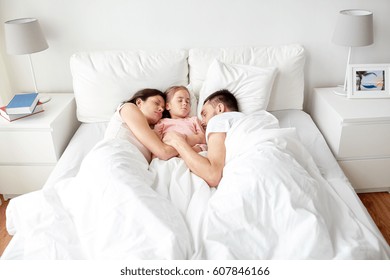 people, family and rest concept - happy child with parents sleeping in bed at home
