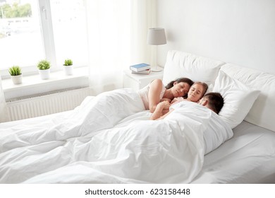 People, Family And Rest Concept - Happy Child With Parents Sleeping In Bed At Home