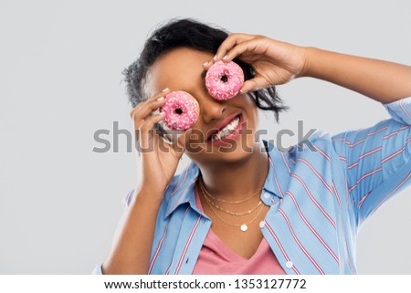 people, fast food and fun concept - happy african american young woman with donuts instead of eyes over grey background