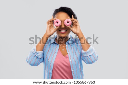 people, fast food and fun concept - happy african american young woman with donuts instead of eyes over grey background