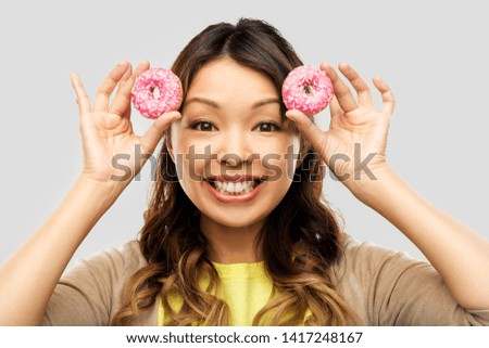 people, fast food and fun concept - happy asian young woman with donuts over grey background