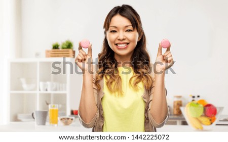 people, fast food and fun concept - happy asian young woman with macarons over home kitchen background
