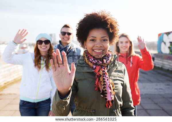 people, friendship and international concept -\
happy african american young woman or teenage girl in front of her\
friends waving hands on city\
street