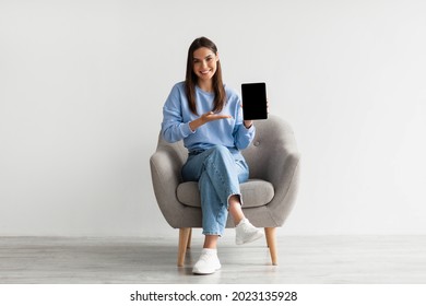 People and gadgets. Happy Caucasian lady showing laptop with blank screen for your website, presenting touch pad with mockup, sitting in armchair against white studio wall, full length - Shutterstock ID 2023135928
