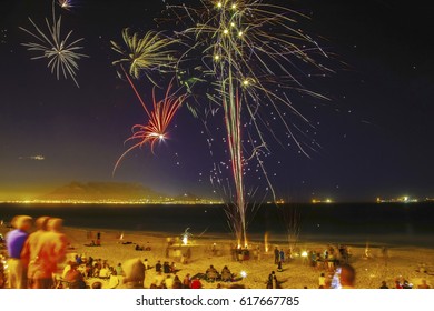 People Gathering On This Famous Beach With Table Mountain In The Background To View The Colorful Fireworks.