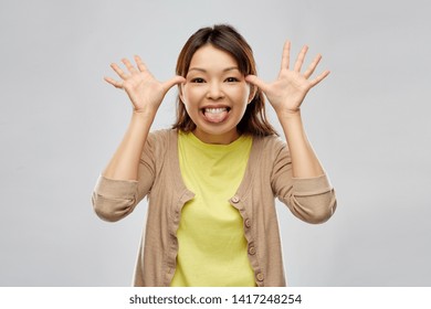 People, Gesture And Fun Concept - Funny Asian Woman Making Silly Faces Over Grey Background