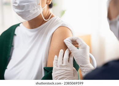 People getting a vaccination to prevent pandemic concept. Mature Woman in medical face mask  receiving a dose of immunization coronavirus vaccine from a nurse at the medical center hospital - Shutterstock ID 2385069599