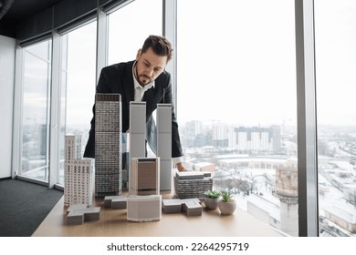 People, global business, company worker concept. Portrait of confident bearded businessman real estate agent in formal clothes, looking at building complex prototype project of 3d city model at table - Powered by Shutterstock